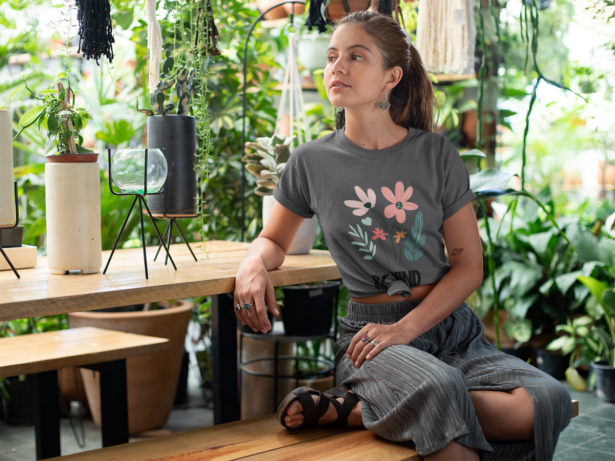 Model wearing a graohite heather tee with a floral “Be Kind” design against a neutral background.