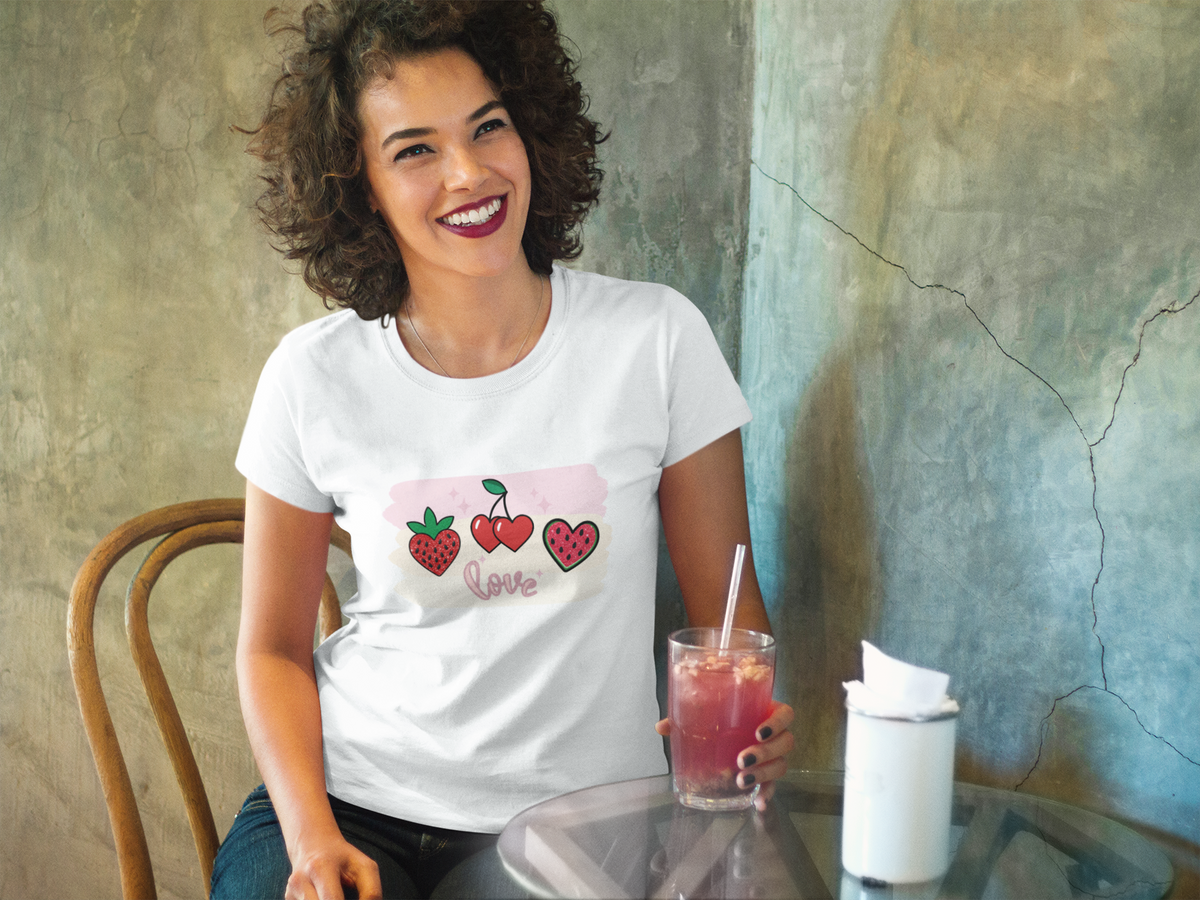 Model outdoors wearing a white T‑shirt featuring a strawberry, cherry, and watermelon slice above the word ‘Love’ in cursive.