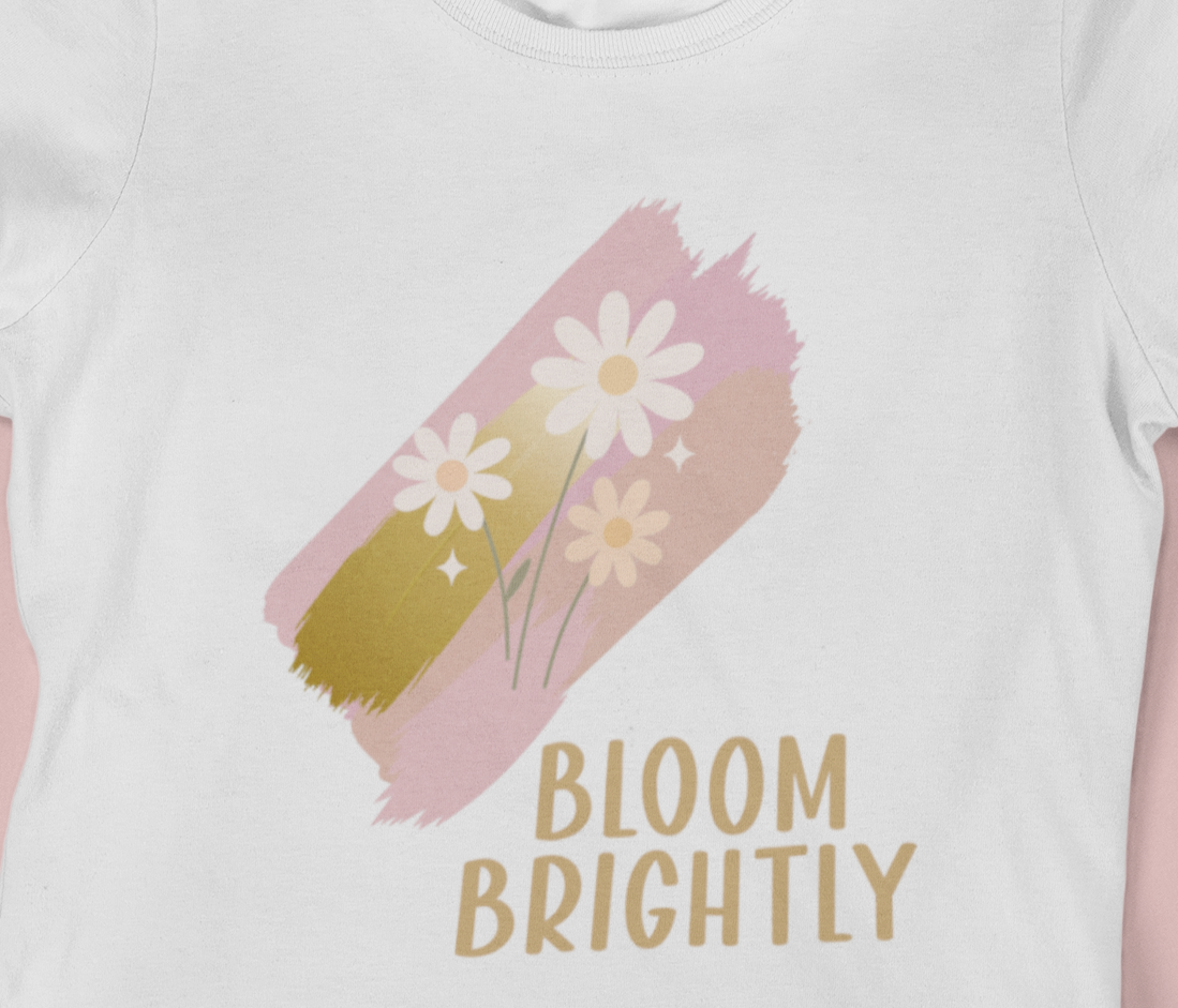 Close‑up of the pastel brushstroke daisy artwork and Bloom Brightly lettering on a white t‑shirt.