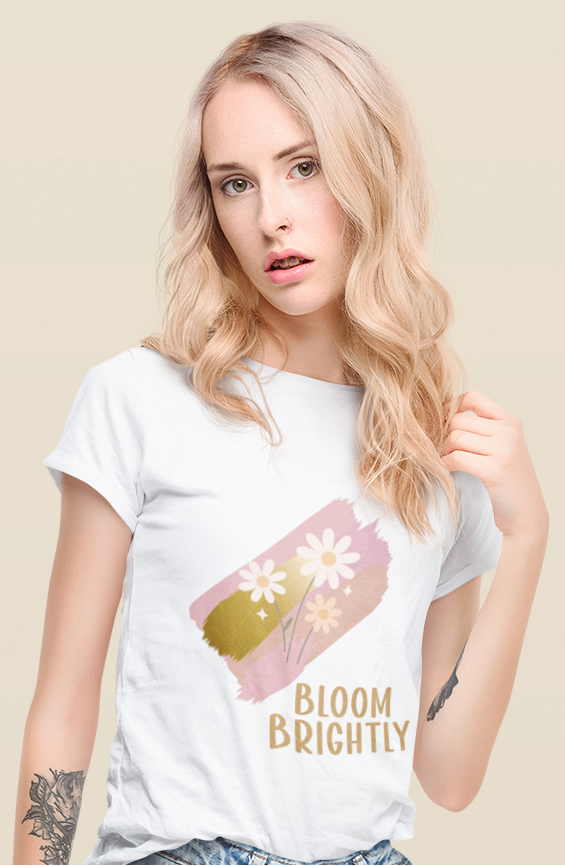 White t‑shirt worn by a woman featuring a pastel brushstroke daisy motif and Bloom Brightly message.