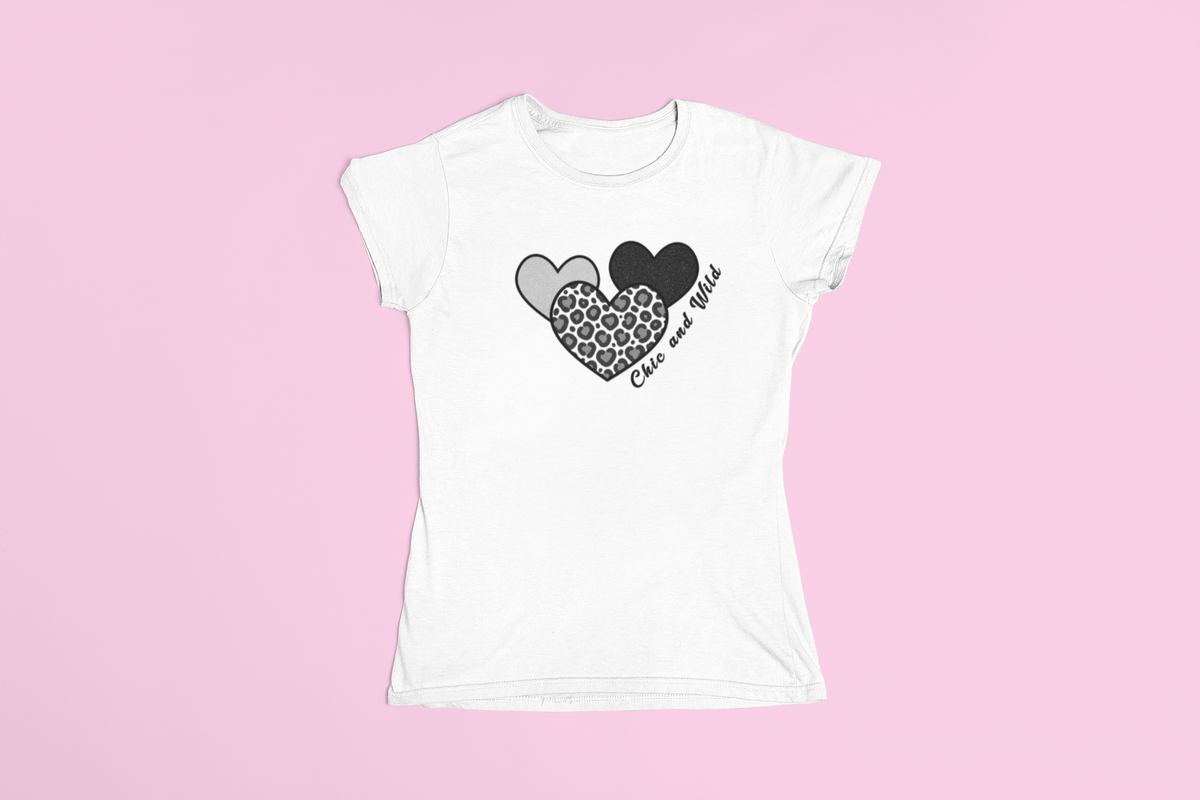 White T‑shirt laid flat on a pink background showing three hearts—black, leopard print, and grey—with the words ‘Cute and Wild’ across the design.