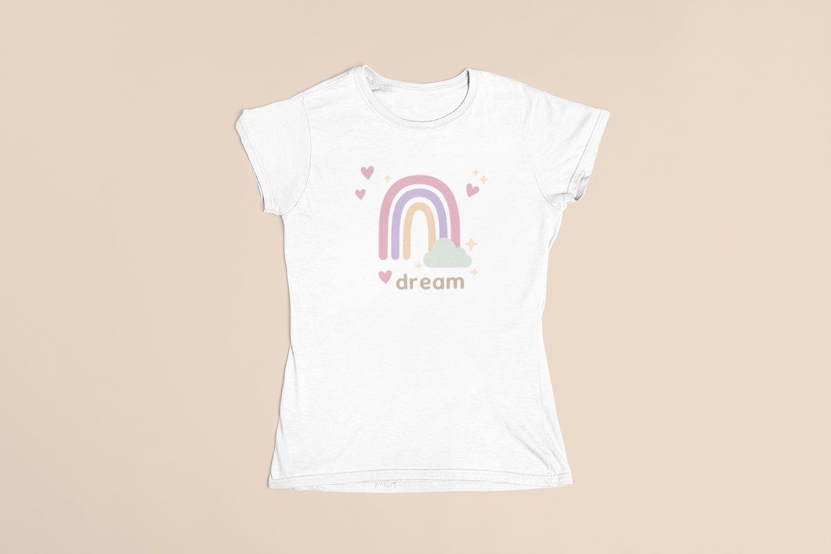 White tee flat lay featuring a soft pastel rainbow, tiny hearts, and “dream” typography in a clean boutique layout.