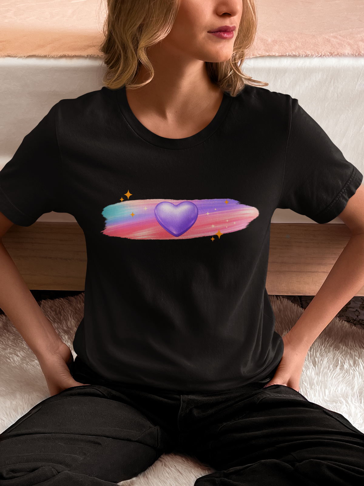 Woman wearing a black t‑shirt with a glowing purple heart design surrounded by soft pastel brushstrokes and sparkle accents.
