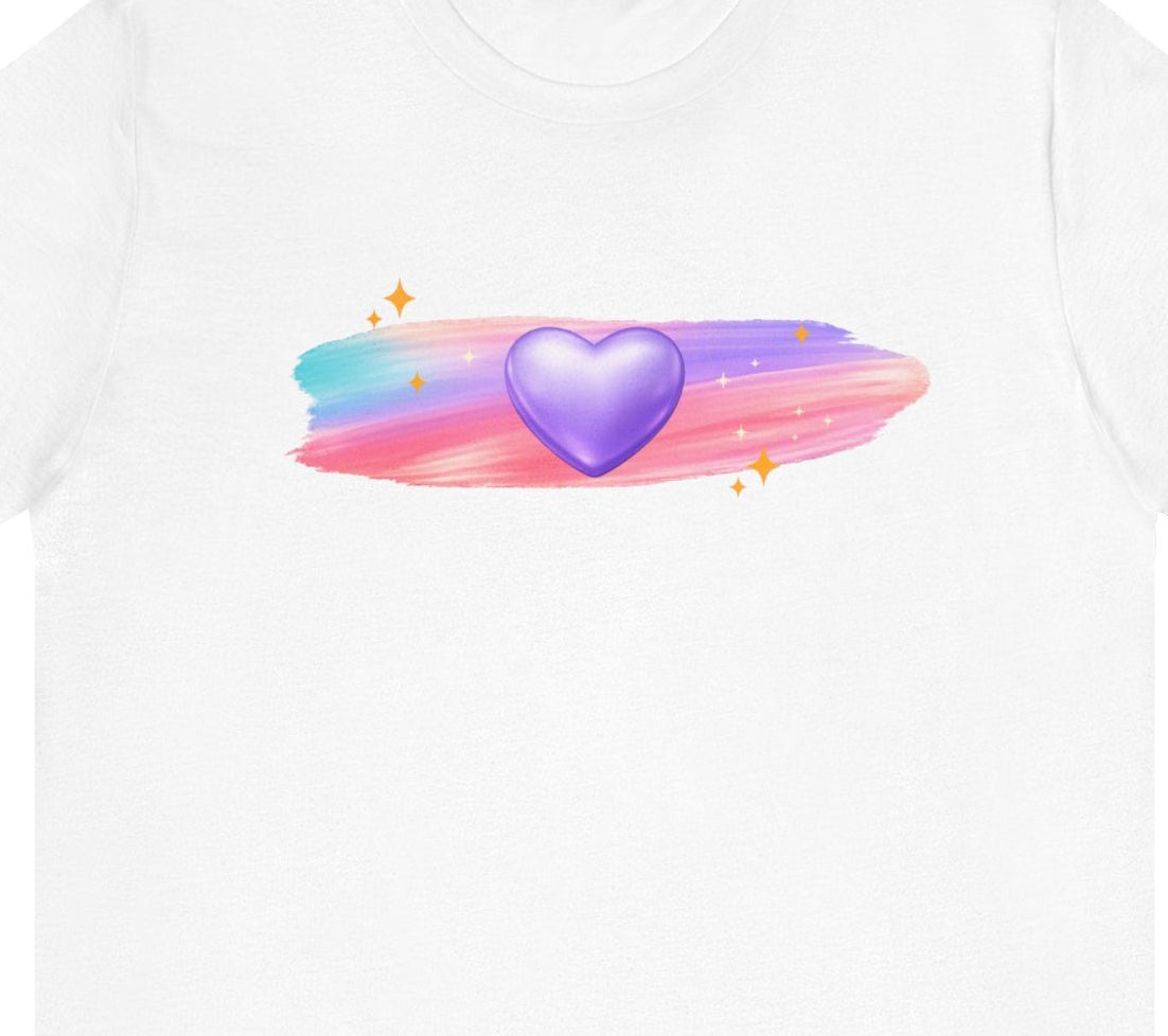 Angled flat lay of a white t‑shirt featuring a glowing purple heart with soft pastel brushstrokes and subtle sparkle accents.