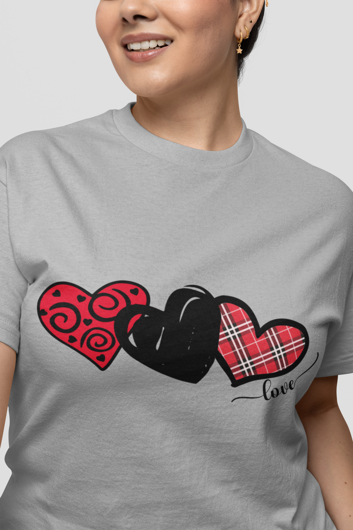 Model wearing a light grey T‑shirt featuring three decorative red and black hearts across the chest.