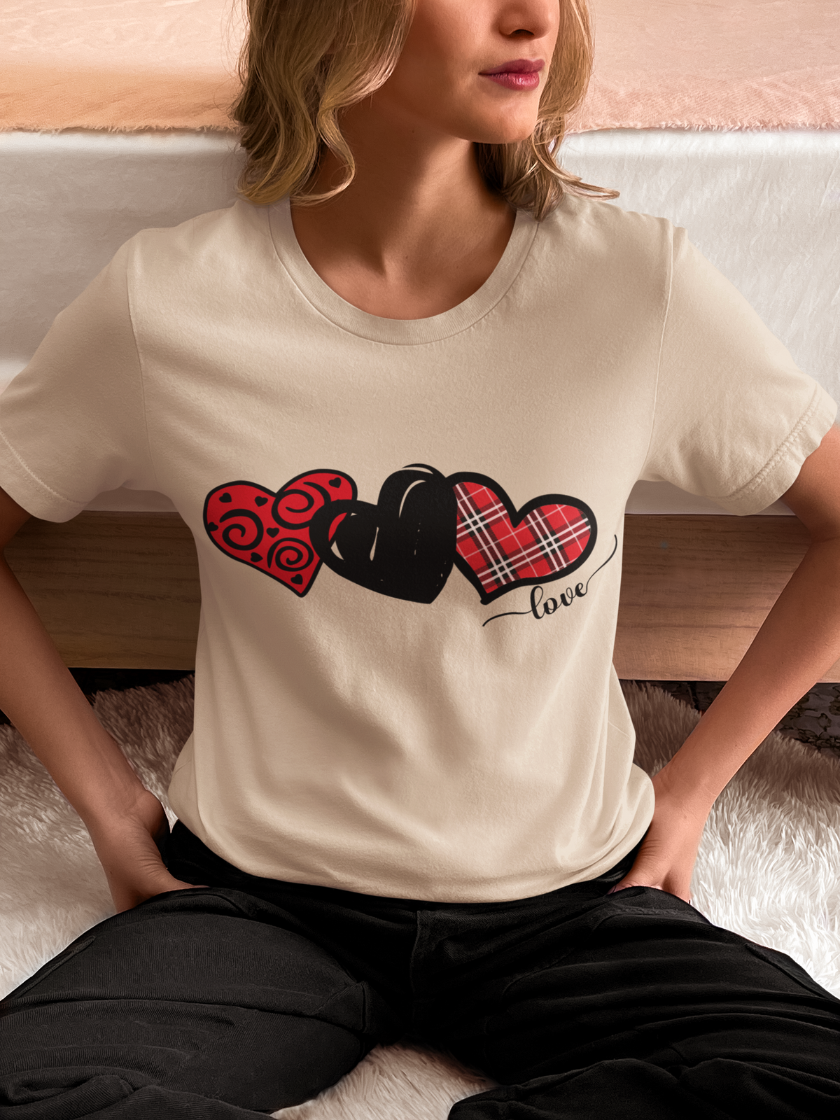 Model wearing a sand T‑shirt with three patterned red and black hearts arranged in a row.