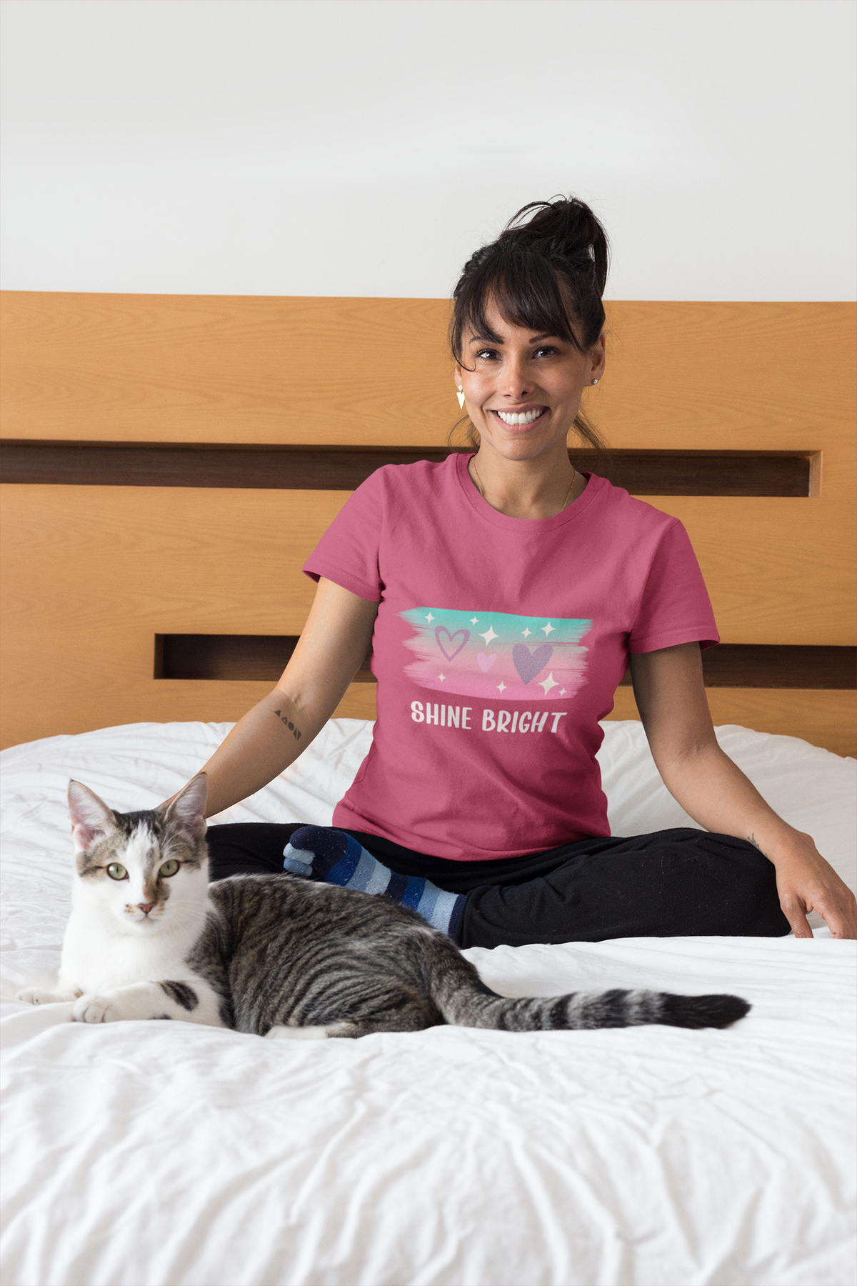Model sitting on a bed wearing the berry Shine Bright Pastel Tee with pastel stars and heart motif.