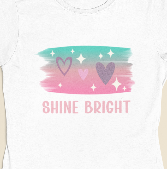 Close‑up of the Shine Bright Pastel Tee design showing pastel brush strokes, stars, hearts, and SHINE BRIGHT text.